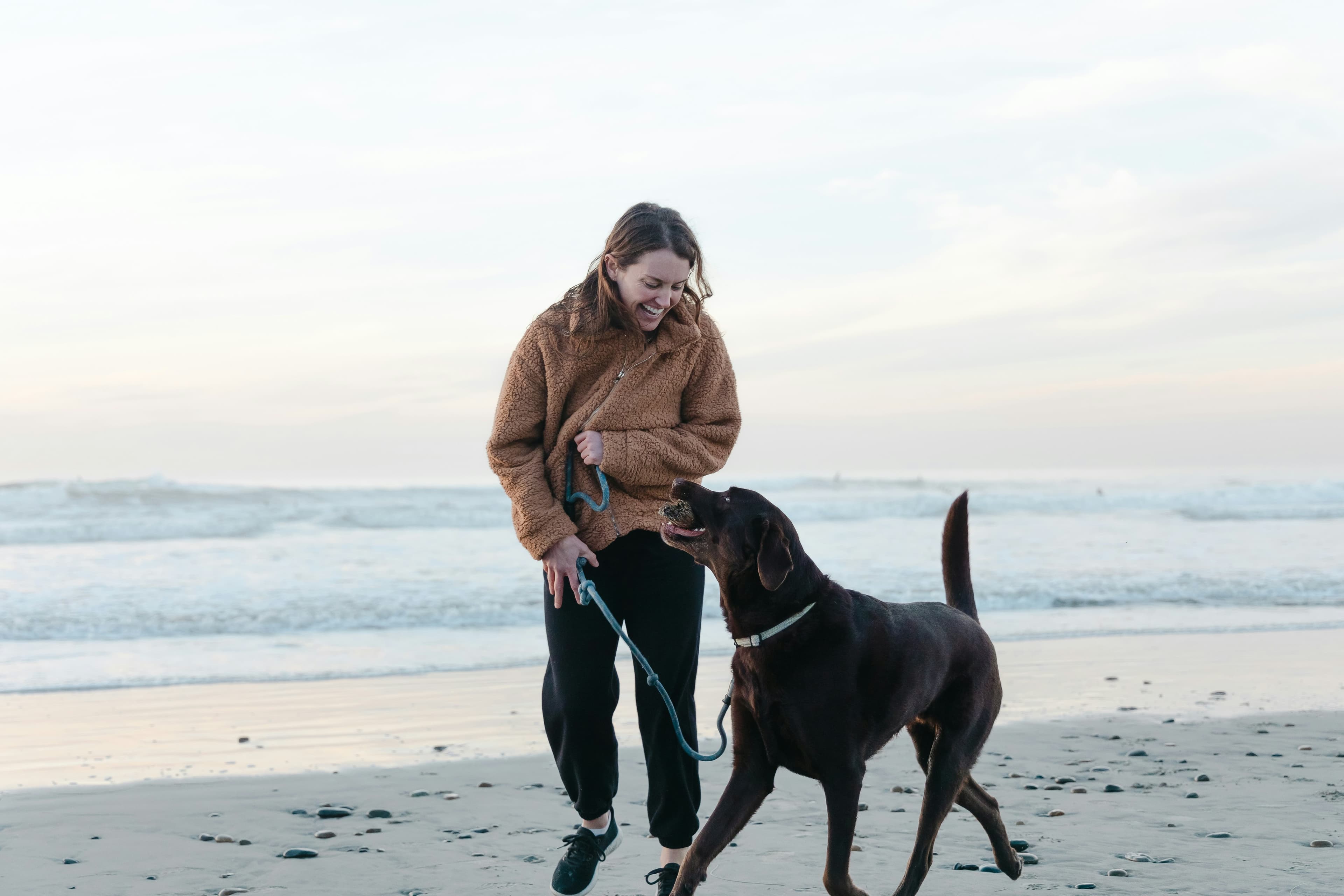 Woman smiling at dog whilst walking on beach on leash